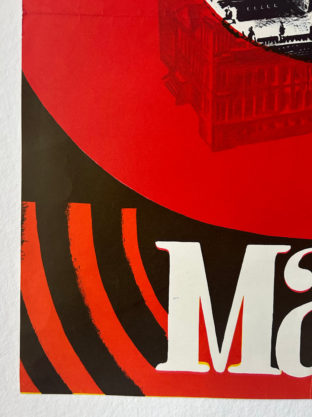 A close-up of a graphic poster print featuring a bold red and black design with large white letters and a black-and-white building illustration in the upper right.