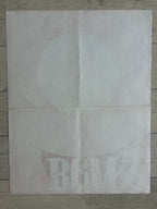A square white sheet of paper with faint red speckled text and a faint circular graphic, laid flat on a gray wood plank surface.