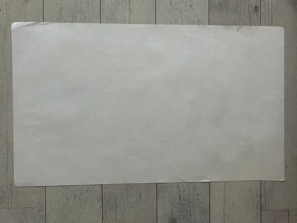 A large, blank, off-white rectangular sheet of paper or cardstock placed flat on a gray wood-plank floor.