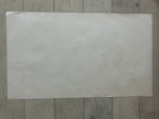 A large, blank, off-white rectangular sheet of paper or cardstock placed flat on a gray wood-plank floor.