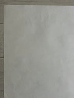 A plain off-white sheet of paper or thin board photographed from above on a light wood surface.