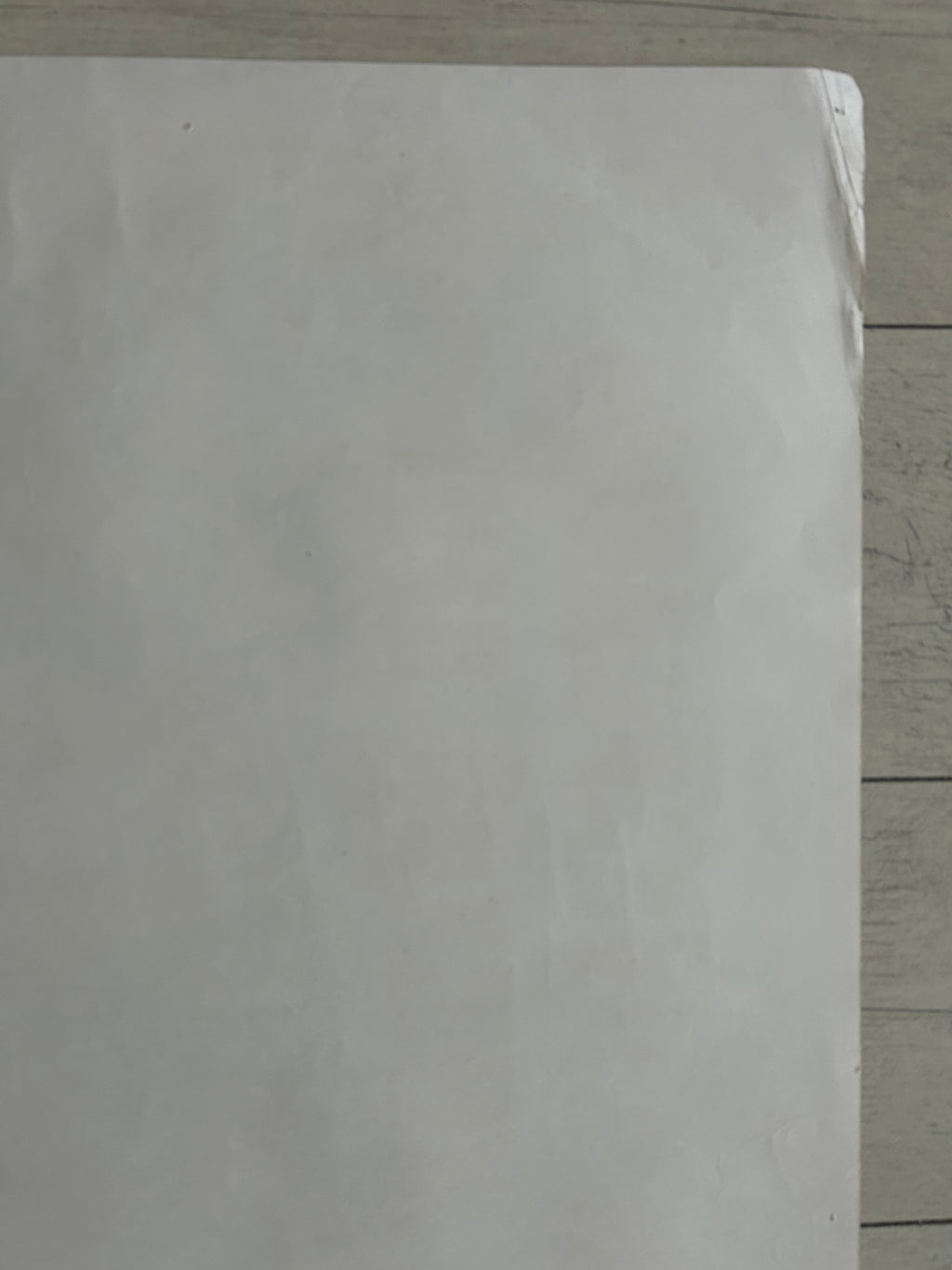A plain white sheet of paper or a blank card lying on a light wood floor.