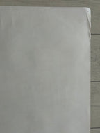 A plain white sheet of paper or a blank card lying on a light wood floor.