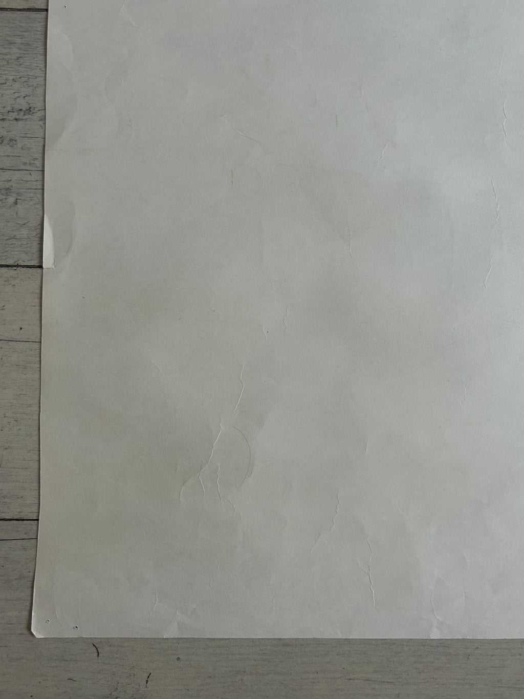 A large, slightly textured off-white sheet of paper or cardstock laid flat on a light gray wooden surface.