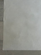 A large, slightly textured off-white sheet of paper or cardstock laid flat on a light gray wooden surface.