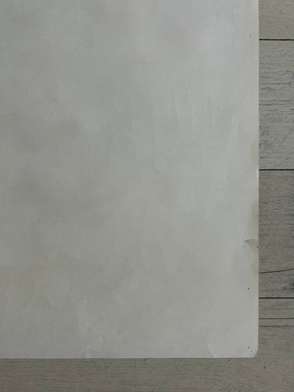 A blank, textured off-white square card or paper sheet placed on a light gray wooden surface.