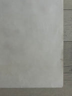 A blank, textured off-white square card or paper sheet placed on a light gray wooden surface.