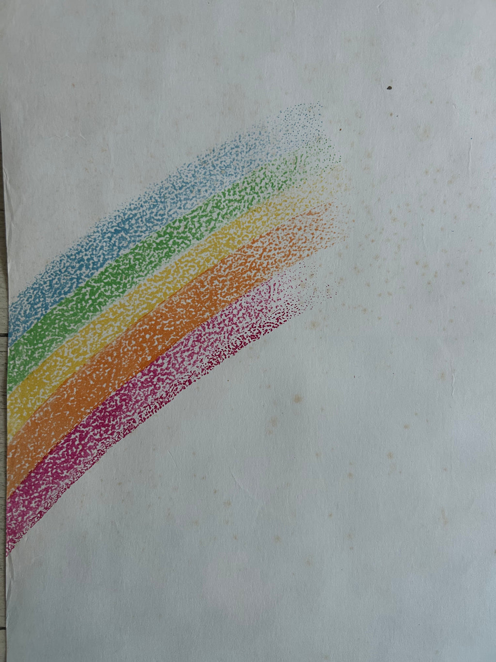 A rainbow-colored dotted pattern, likely a crayon or pastel pencil swatch, on a textured off-white paper background.