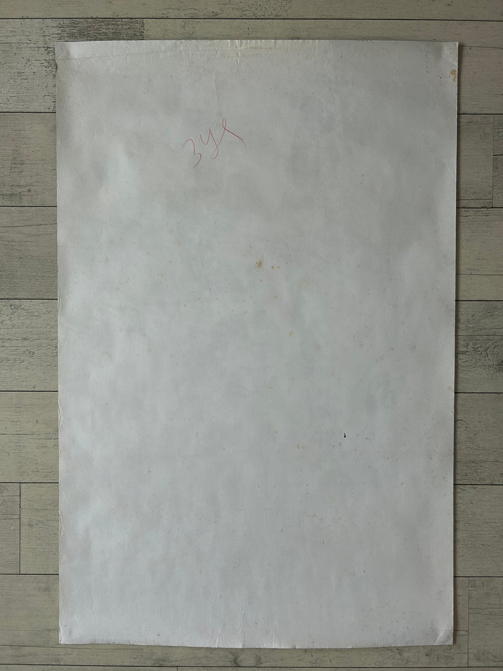 A large, blank off-white sheet of paper or cardstock with a faint red handwritten '3x4' in the upper left, laid flat on a light gray wood plank surface.