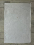A large, blank off-white sheet of paper or cardstock with a faint red handwritten '3x4' in the upper left, laid flat on a light gray wood plank surface.