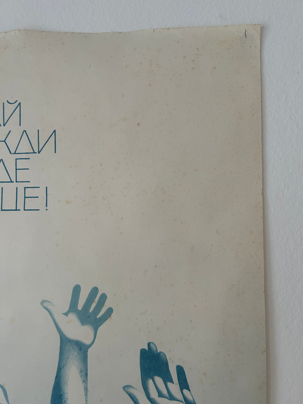 A vintage Soviet propaganda poster mounted on a white wall, featuring blue Cyrillic text and illustrations of raised hands on a beige background.