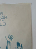 A vintage Soviet propaganda poster mounted on a white wall, featuring blue Cyrillic text and illustrations of raised hands on a beige background.
