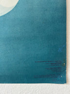 A vintage Indonesian educational poster or print featuring a teal blue background with white curved graphic elements in the top-left corner and small printed text near the bottom right, displayed against a white textured wall.