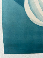 A close-up of a blue-green printed paper corner with a white curved stripe detail, photographed against a white textured background.