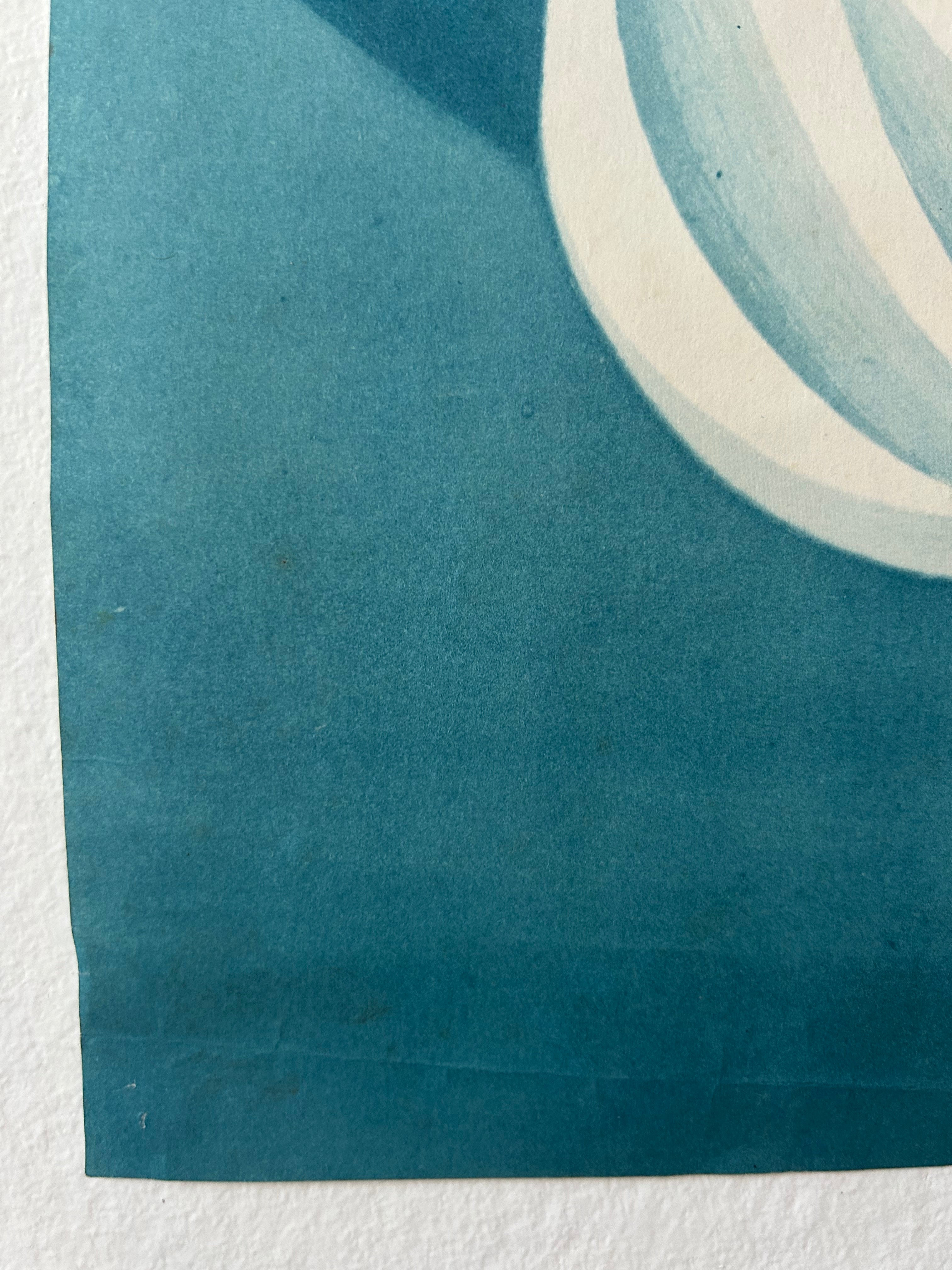A close-up of a blue-green printed paper corner with a white curved stripe detail, photographed against a white textured background.