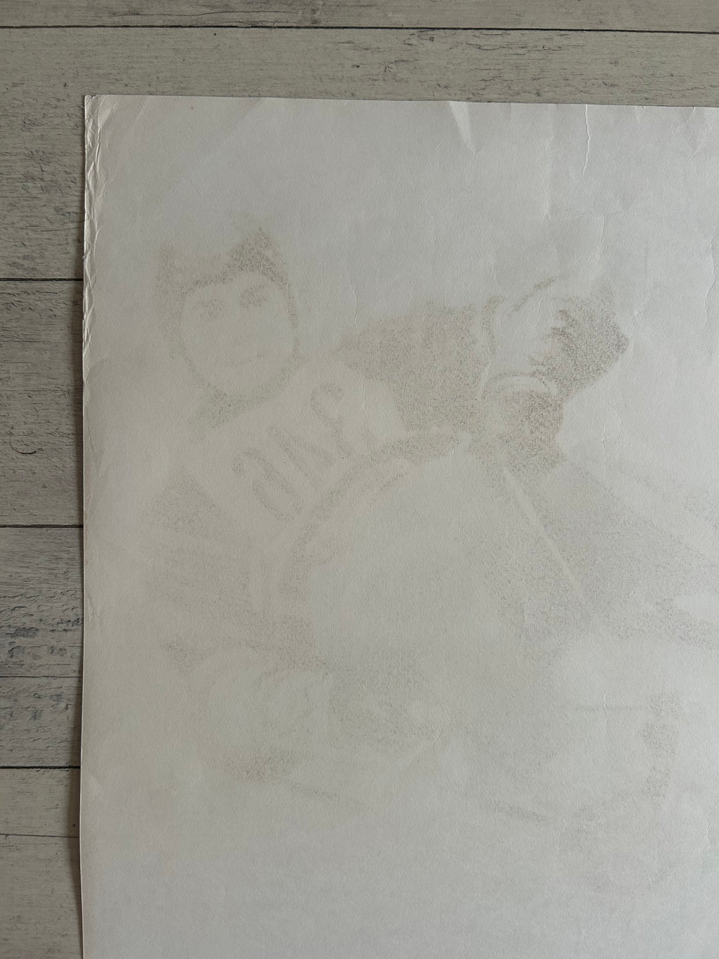 A square off-white art print or poster featuring a faint, low-contrast portrait sketch of a person in a baseball uniform, laid flat on a gray wood plank surface.
