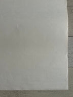 A large sheet of white or off-white paper laid flat on a light gray wood surface, filling most of the frame.
