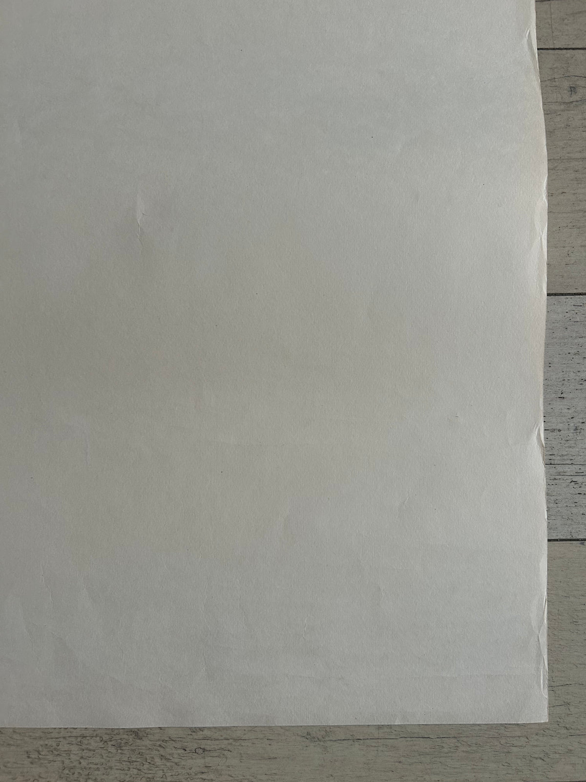 A large sheet of white or off-white paper laid flat on a light gray wood surface, filling most of the frame.