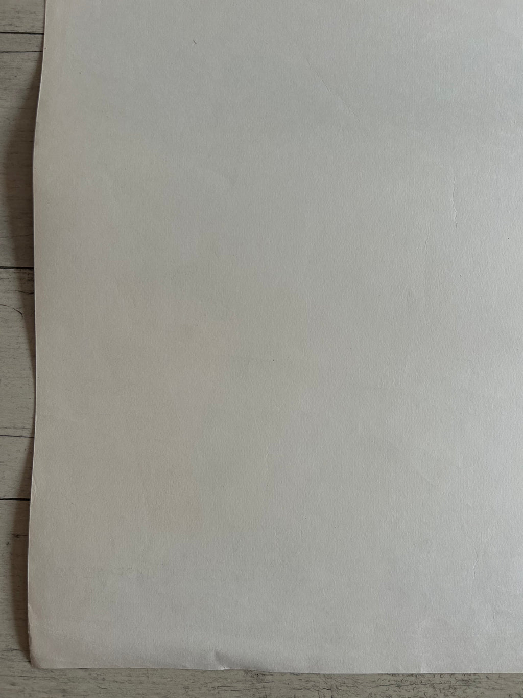 A blank, off-white sheet of paper or cardstock laid flat on a light-colored wooden surface.