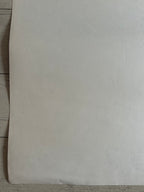 A blank, off-white sheet of paper or cardstock laid flat on a light-colored wooden surface.