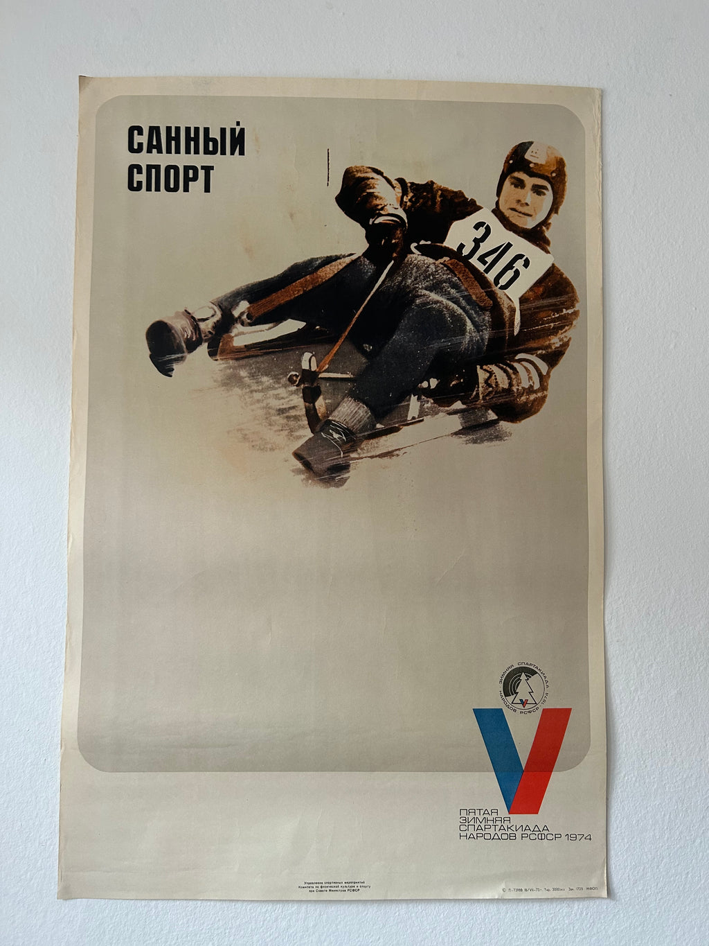 A vintage Soviet sports poster for winter sports, featuring a skater in action with the text 'СТКАННО СЛОВО' at the top and a stylized red and blue 'V' logo at the bottom, displayed against a light gray wall.