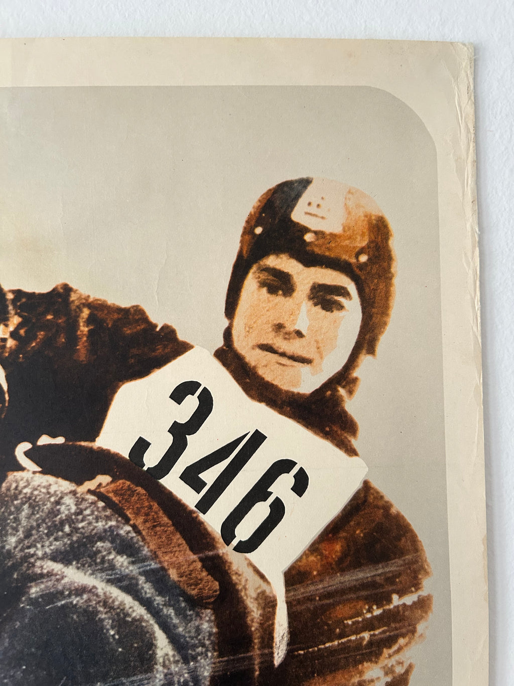 A vintage printed card or photo print showing a person in winter gear holding a bib number 346, with an aged cream border and warm sepia tones.