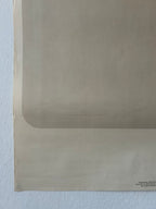 A close-up of a beige or light tan paper sheet with a folded corner, resting against a white textured wall. Small black text is visible in the bottom right corner.