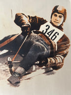 Vintage-style illustration or print of a bobsled racer wearing a brown helmet and jacket, seated in a sled on a snowy track, with a large number 346 on the chest.