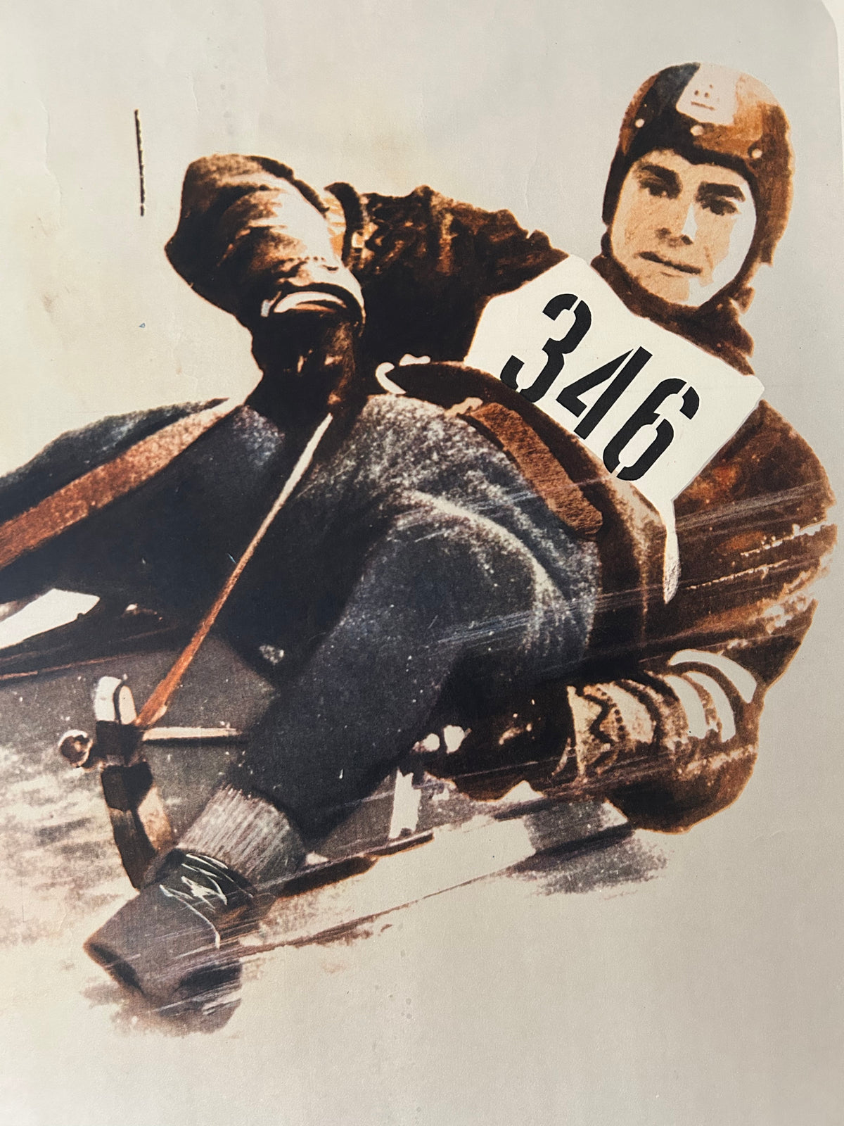 Vintage-style illustration or print of a bobsled racer wearing a brown helmet and jacket, seated in a sled on a snowy track, with a large number 346 on the chest.